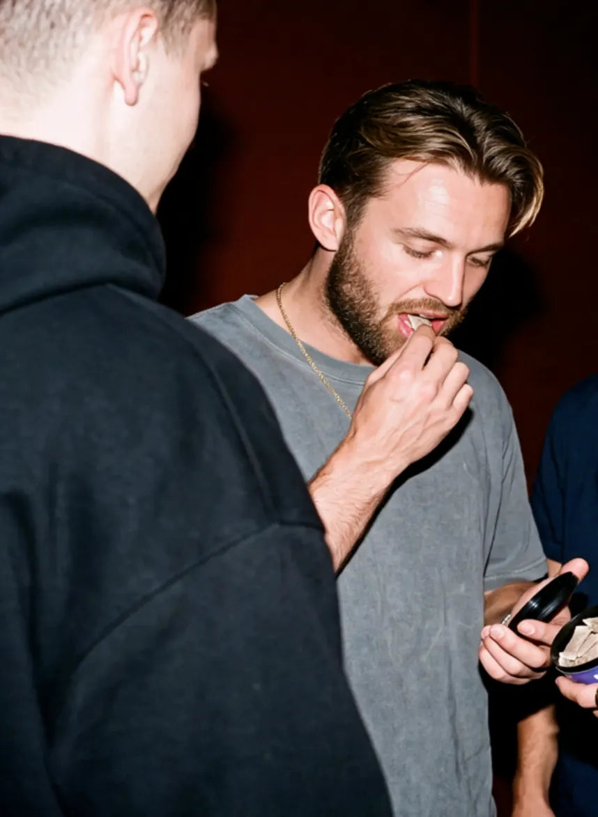 Junger Mann legt sich auf einer Party einen WAVE Pouch unter die Lippe
