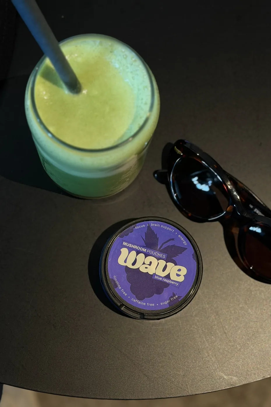 Eine Dose WAVE auf einem dunklen Tisch neben einem grünen Smoothie und einer Sonnenbrille